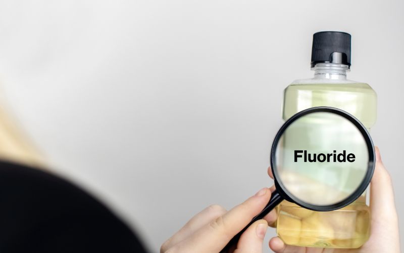person holding a bottle of mouthwash with a magnifying glass which shows the word fluoride
